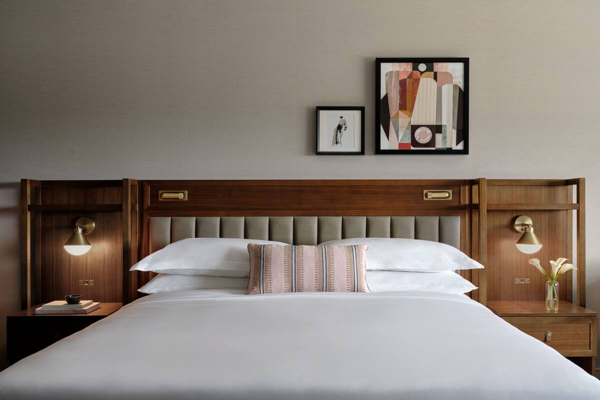 A neatly made bed with a wooden headboard, two bedside tables with lamps, and two framed pictures on the wall.