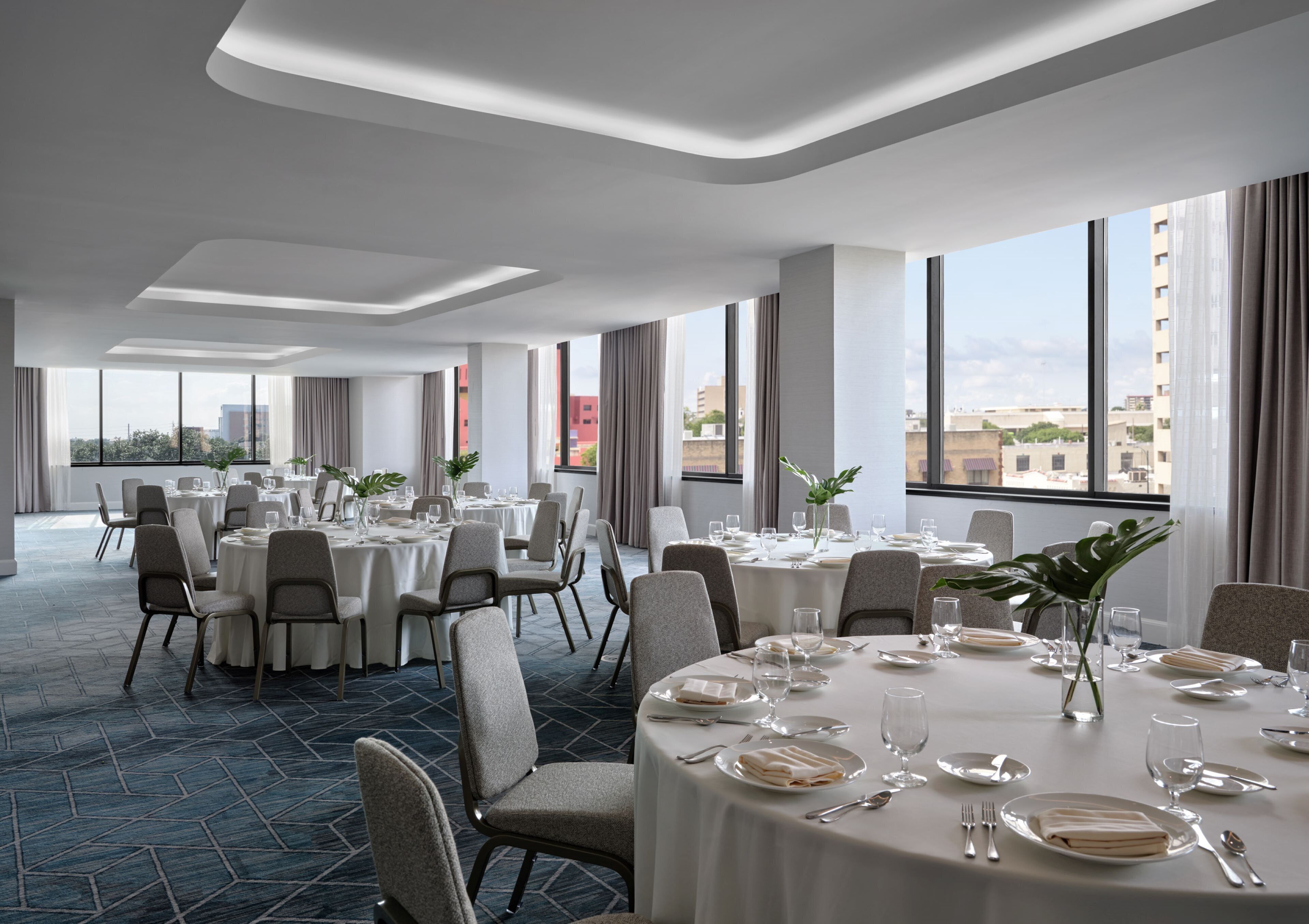 A spacious dining area with round tables, chairs, and large windows offering city views.