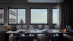 Ein Essbereich mit einem langen Tisch, gedeckt für eine Mahlzeit, großen Fenstern mit Blick auf die Stadtlandschaft und einer modernen Kronleuchter.