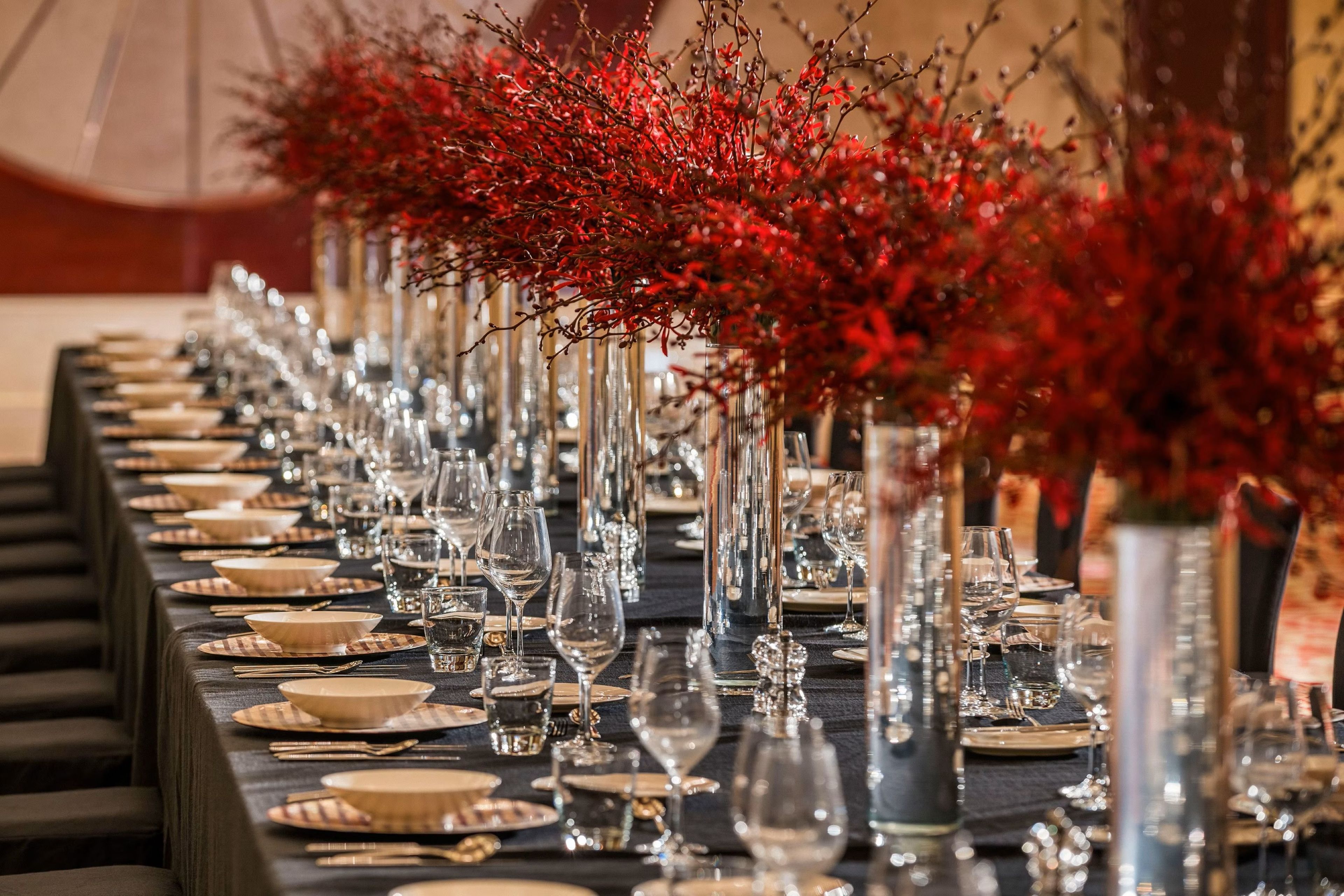 A long dining table set with multiple place settings, including plates, cutlery, and glasses.