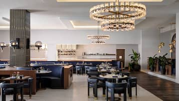 En modern restaurang med ett centralt placerat sittområde, flera bord och en stor kristallkrona.