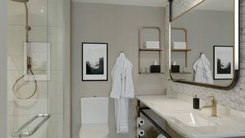 Un baño moderno con ducha de vidrio, inodoro blanco, tocador con grifo dorado y dos cuadros en la pared.