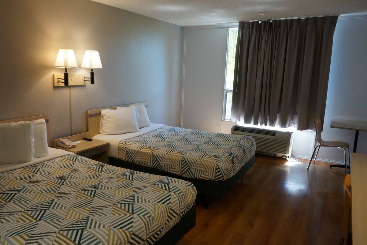 A hotel room with two beds, a nightstand, a telephone, a window with curtains, and a chair.