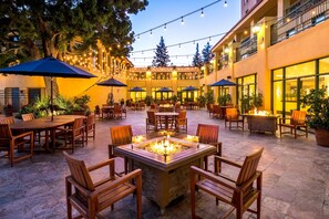Un área de patio al aire libre con mesas y sillas, luces colgantes y un brasero.