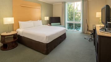 A hotel room with a large bed, a desk with a computer, a chair, a lamp, and a window with curtains.