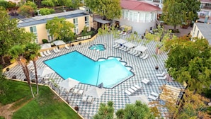 An aerial view of a hotel with a large pool, checkered lounge area, and surrounding greenery.