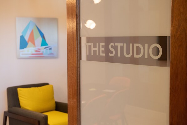 Un área de recepción con un letrero que dice "THE STUDIO" y una silla moderna con un cojín amarillo.
