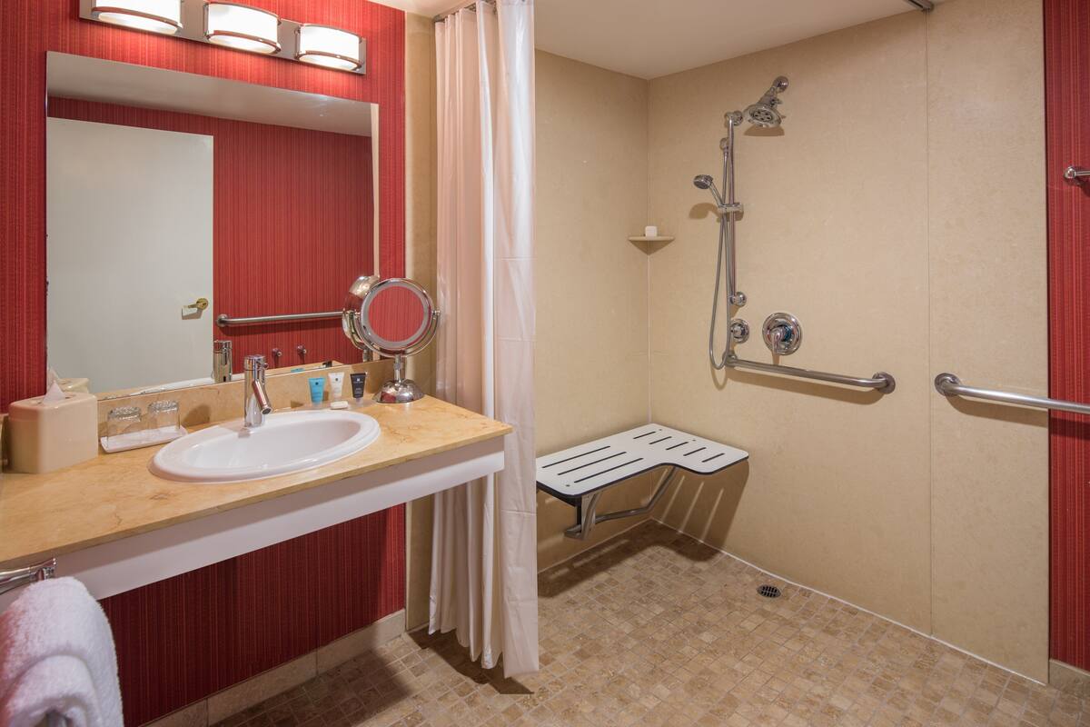 A bathroom with a sink, mirror, shower, and grab bars.