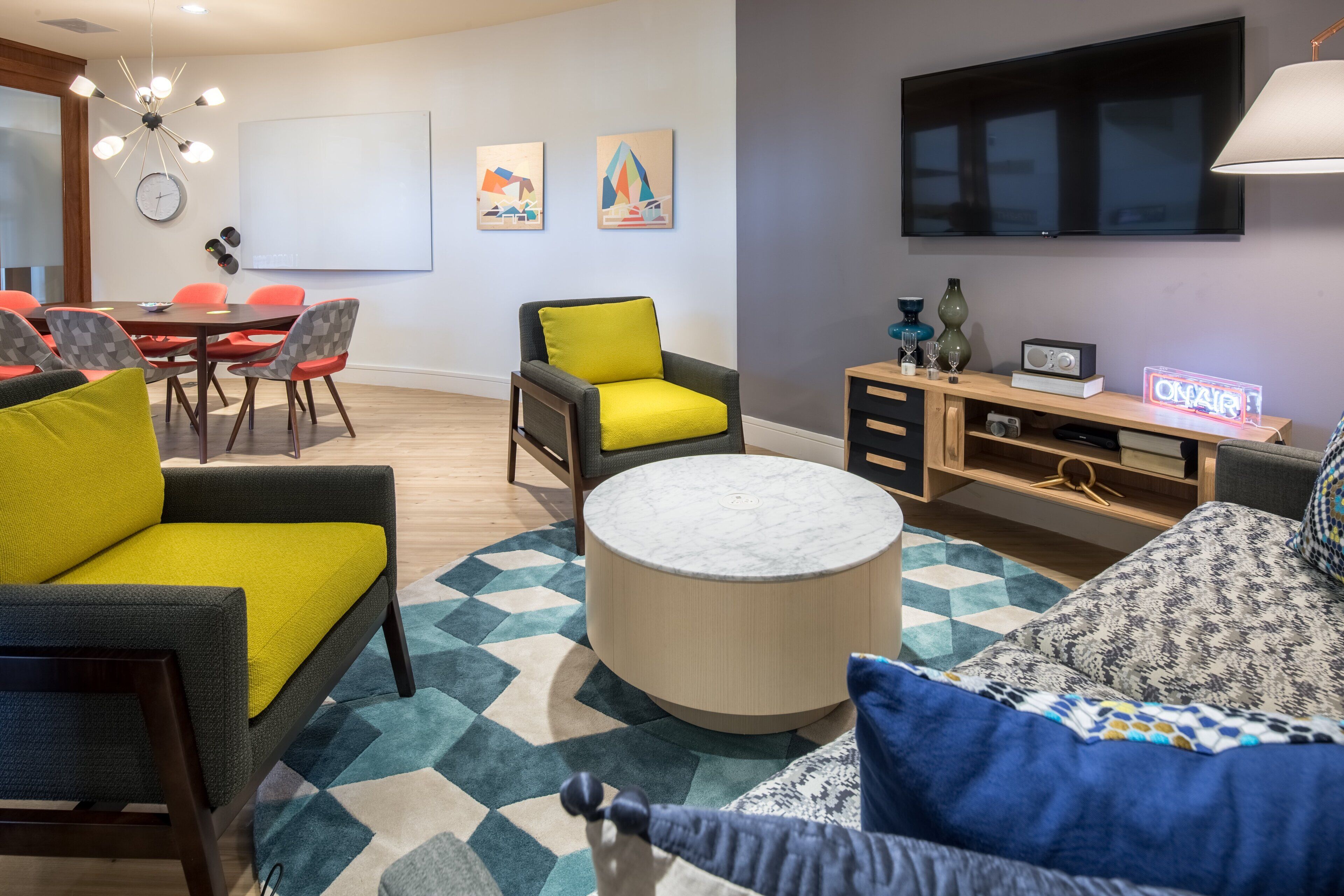 A modern living room with a round coffee table, a sofa, a dining table with chairs, and a flat-screen TV mounted on the wall.