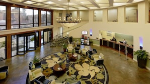 A spacious lobby with a high ceiling, a chandelier, a reception desk, and seating areas.