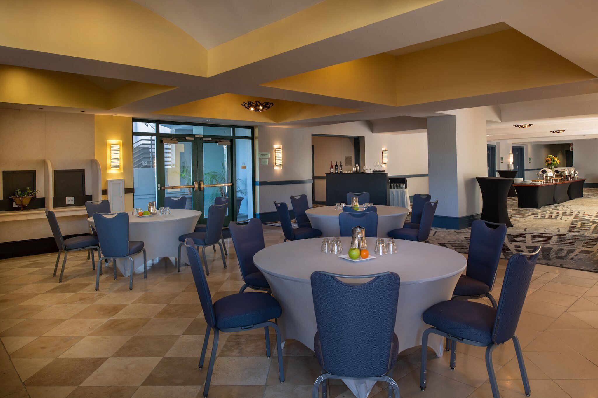 A hotel dining area with round tables, chairs, and a buffet setup.