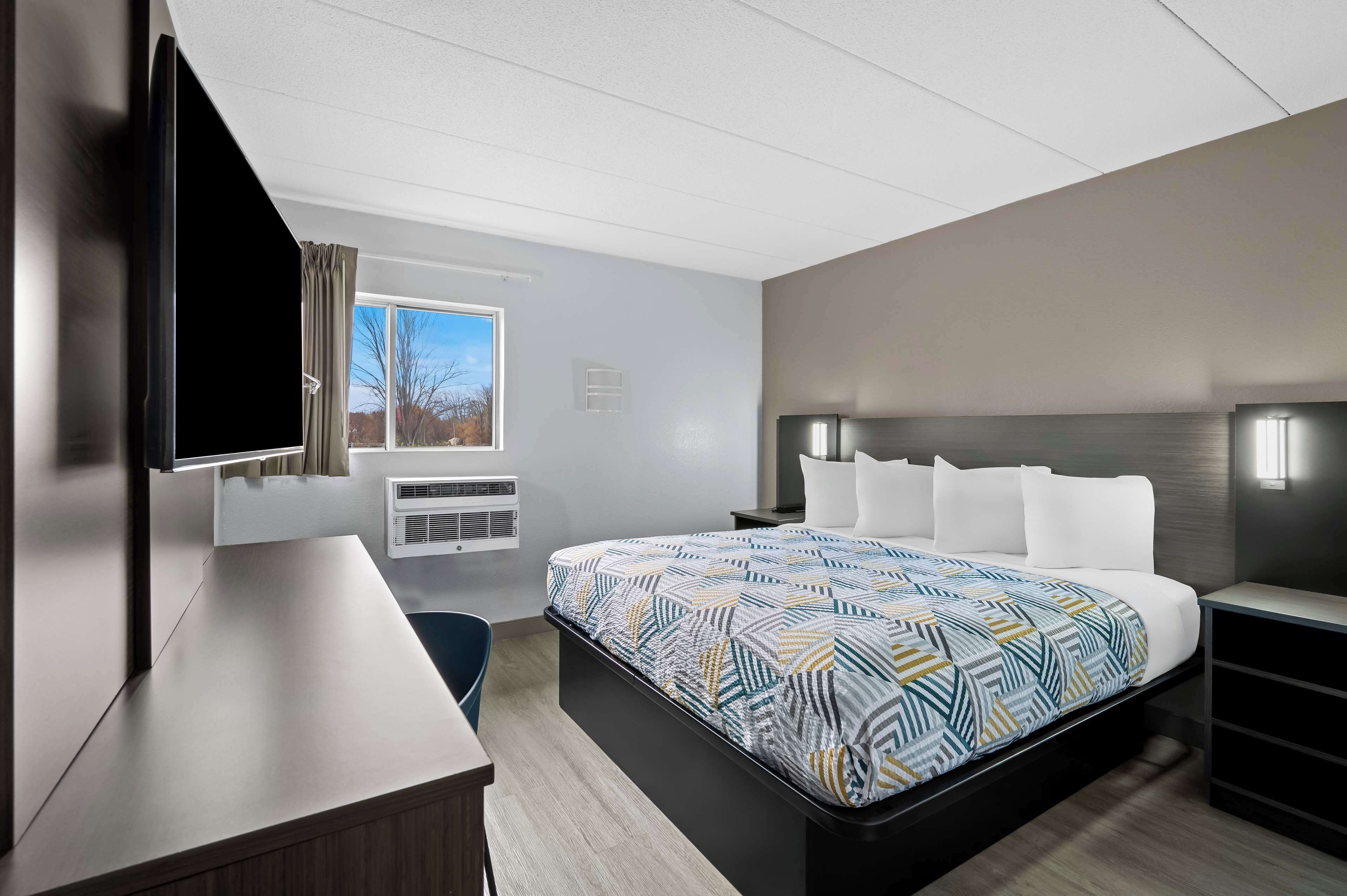 Une chambre d’hôtel moderne dotée d’un grand lit, d’un bureau, d’une télévision à écran plat et d’une fenêtre avec des rideaux.