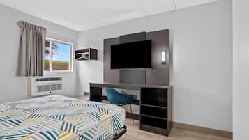 A modern hotel room with a large bed, a desk with a flat-screen TV, and a window with curtains.