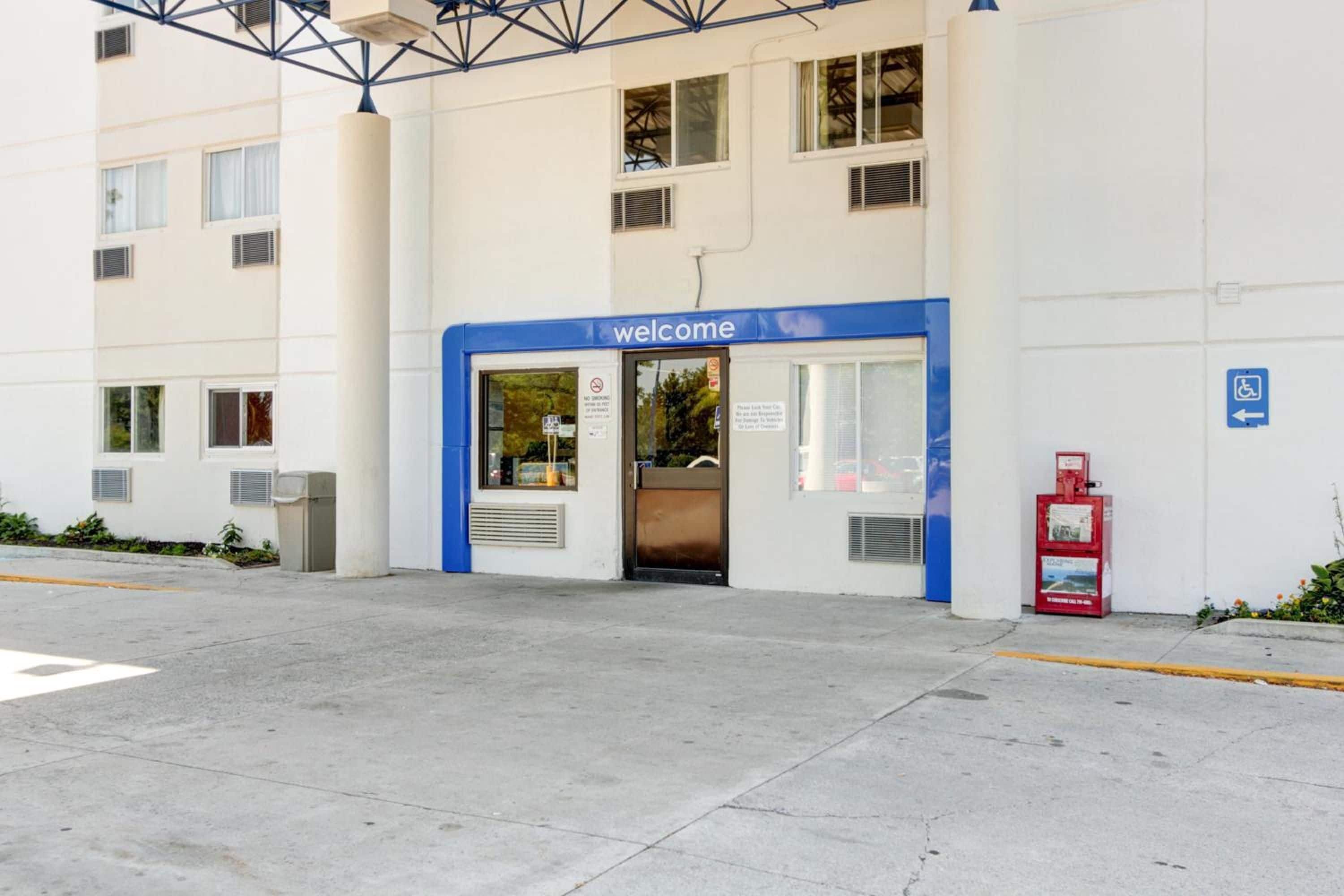 A building entrance with a 'welcome' sign, a blue awning, and a wheelchair accessibility sign.