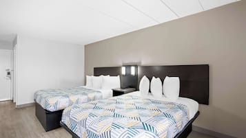 A hotel room with two beds, a dark headboard, a nightstand, and a wall-mounted light fixture.