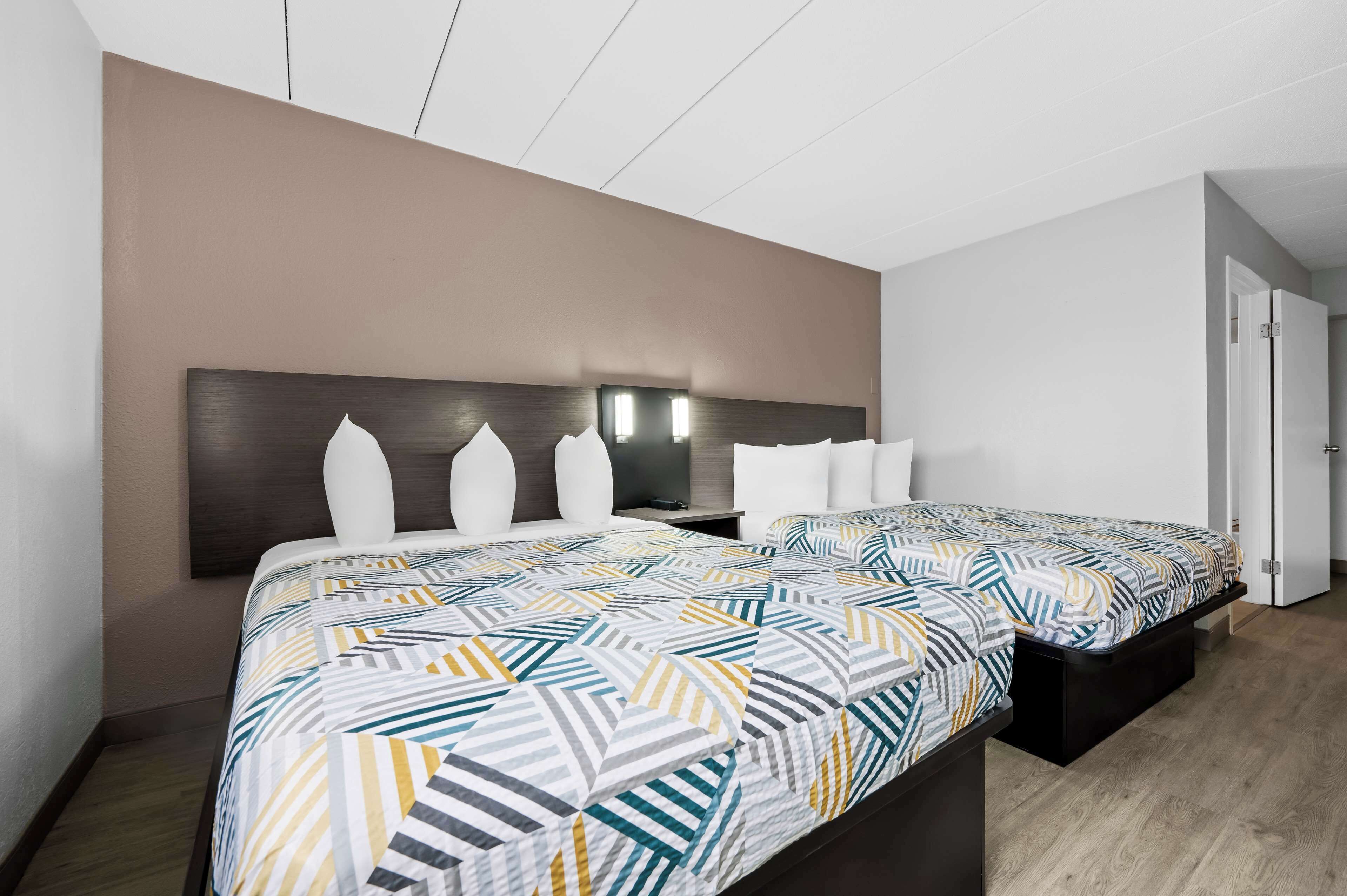 A hotel room with two beds, a dark headboard, and a light-colored wall.