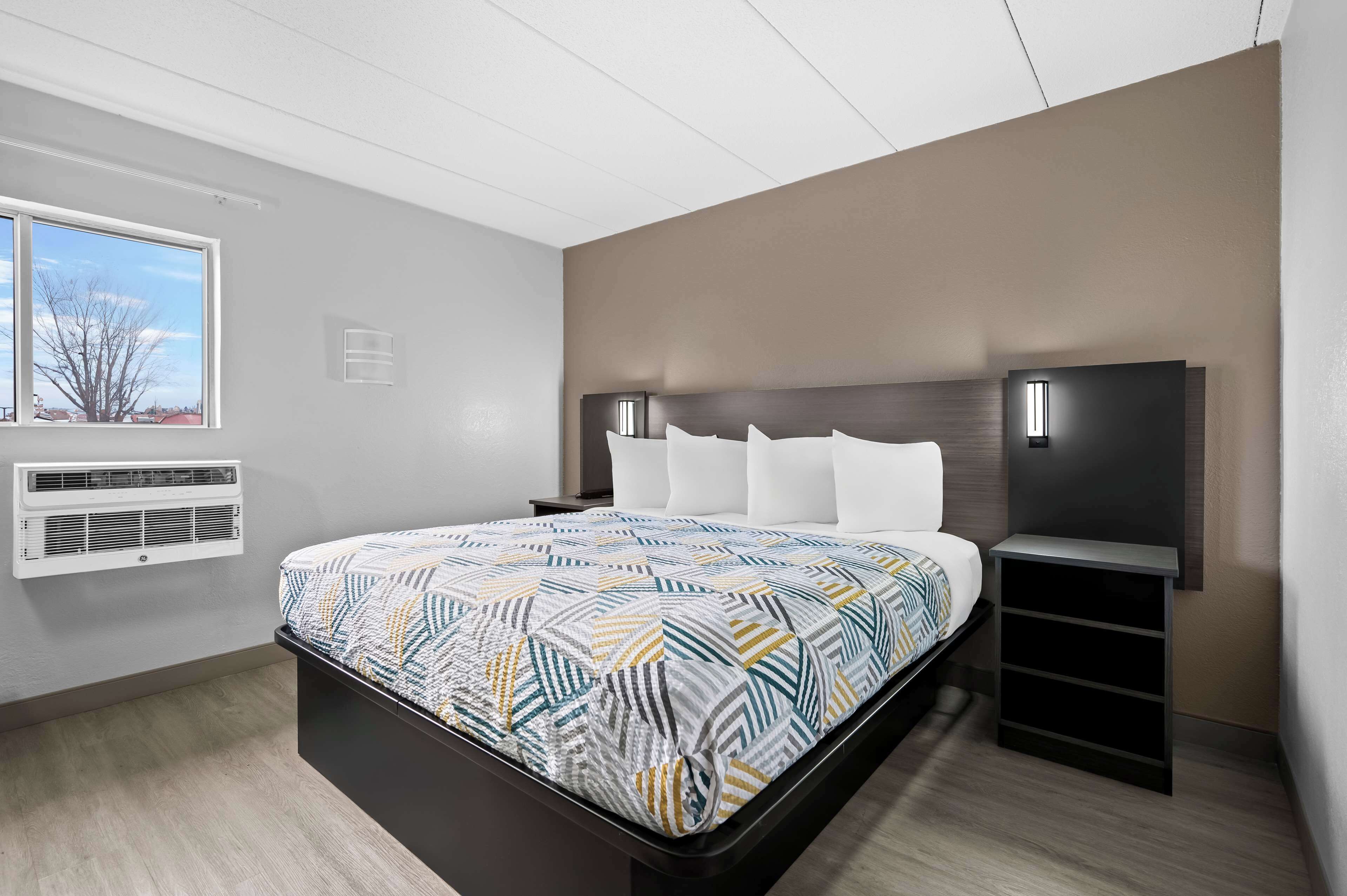 Ein modernes Hotelzimmer mit einem großen Bett, einem an der Wand befestigten Fernseher, einem kleinen Schreibtisch und einem Fenster mit Ausblick.