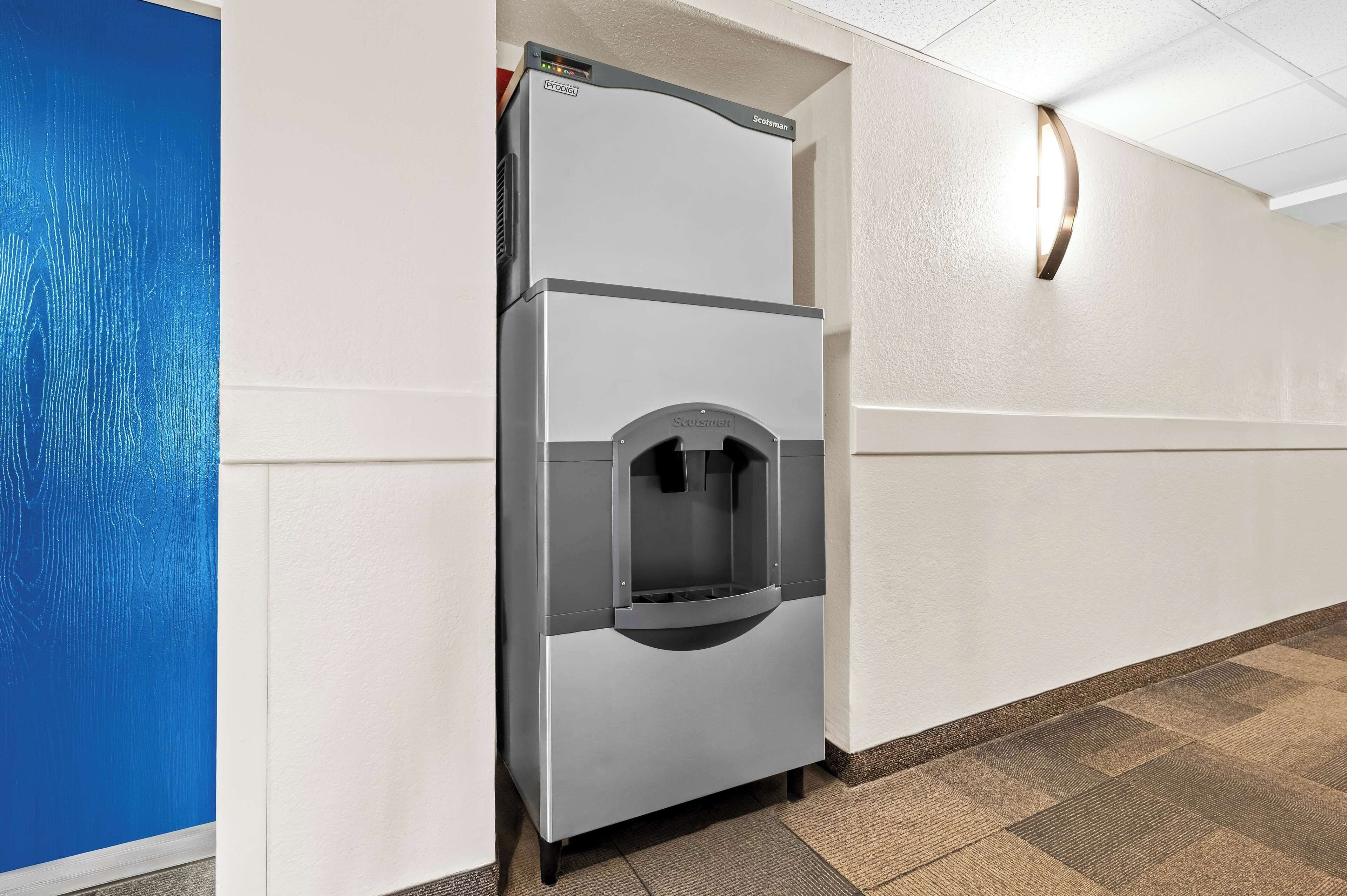 A commercial refrigerator with a water dispenser in a hallway with white walls and a blue door.