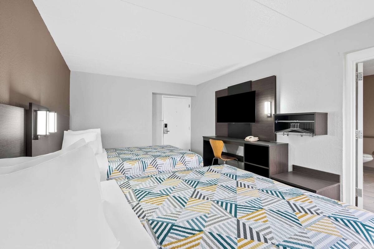 A hotel room with two beds, a desk, a chair, a TV, and a bathroom.