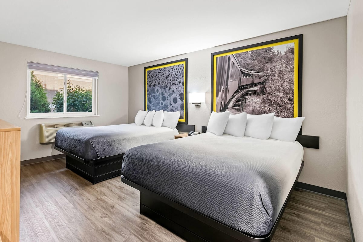 Ein Hotelzimmer mit zwei Betten, einem Fenster und zwei gerahmten Bildern an der Wand.