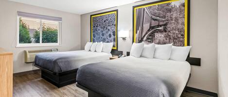 Une chambre d’hôtel avec deux lits, une fenêtre et deux tableaux encadrés au mur.