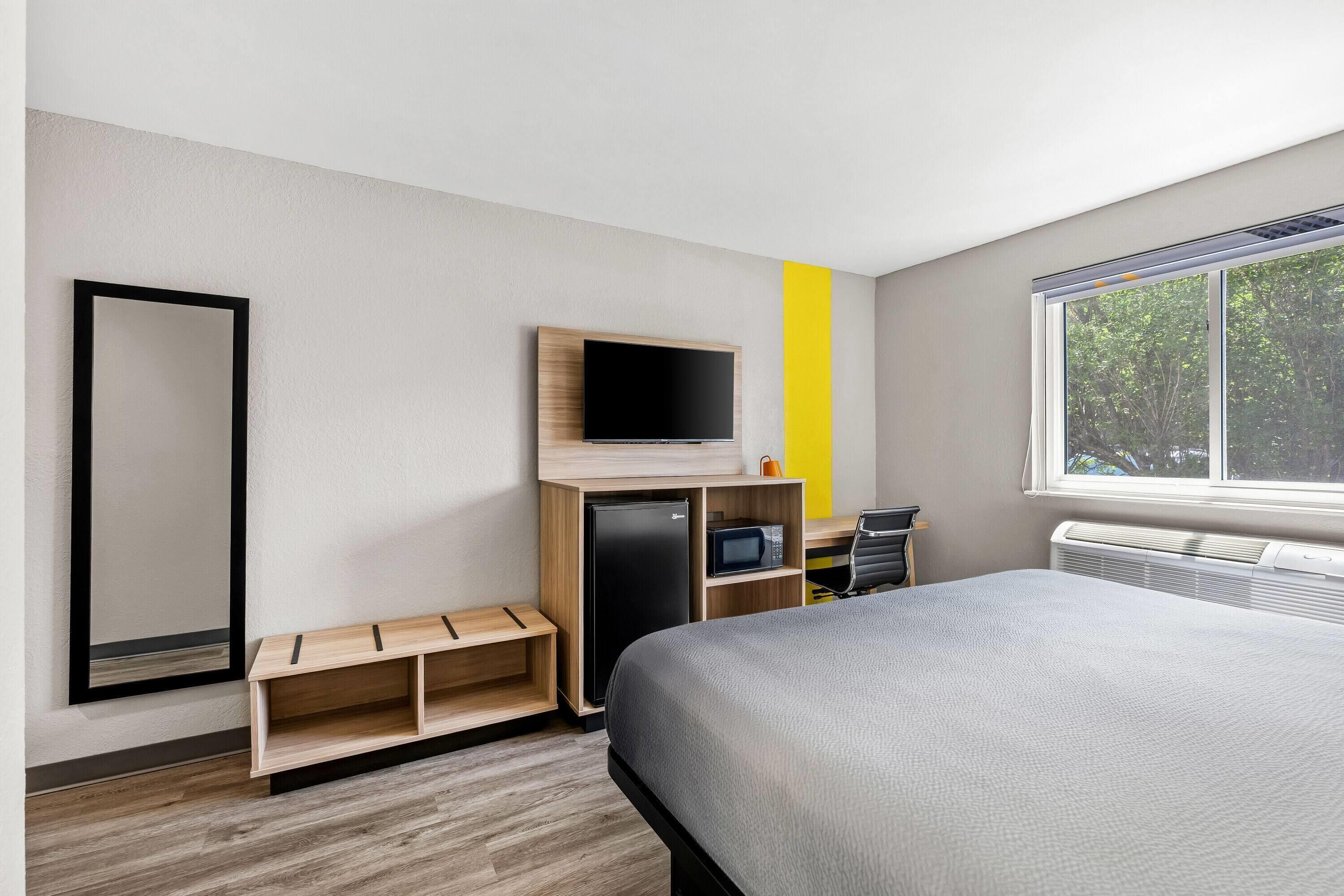 Moderni hotellihuone, jossa on sänky, puuhyllylle asennettu televisio, mikroaaltouuni ja pieni oleskelualue.
