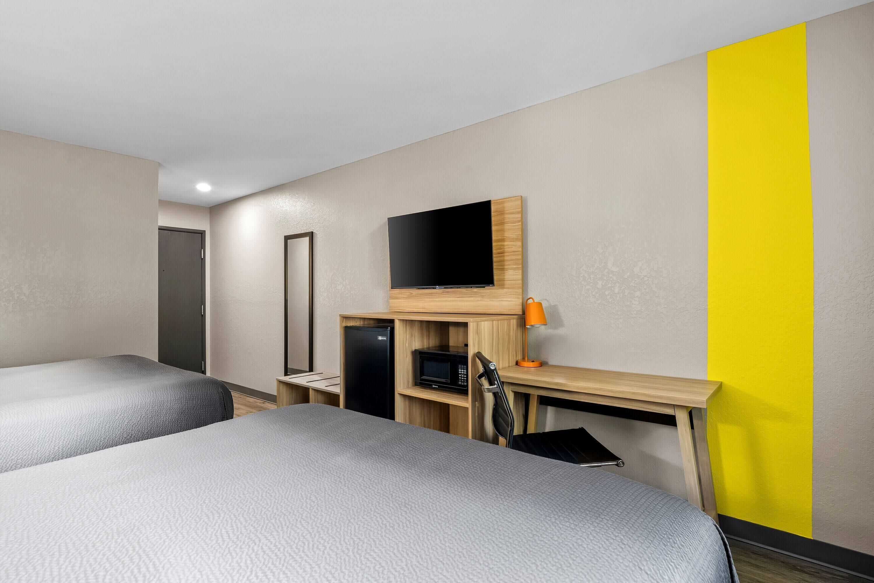 A hotel room with two beds, a flat-screen TV, a microwave, and a desk with a chair.