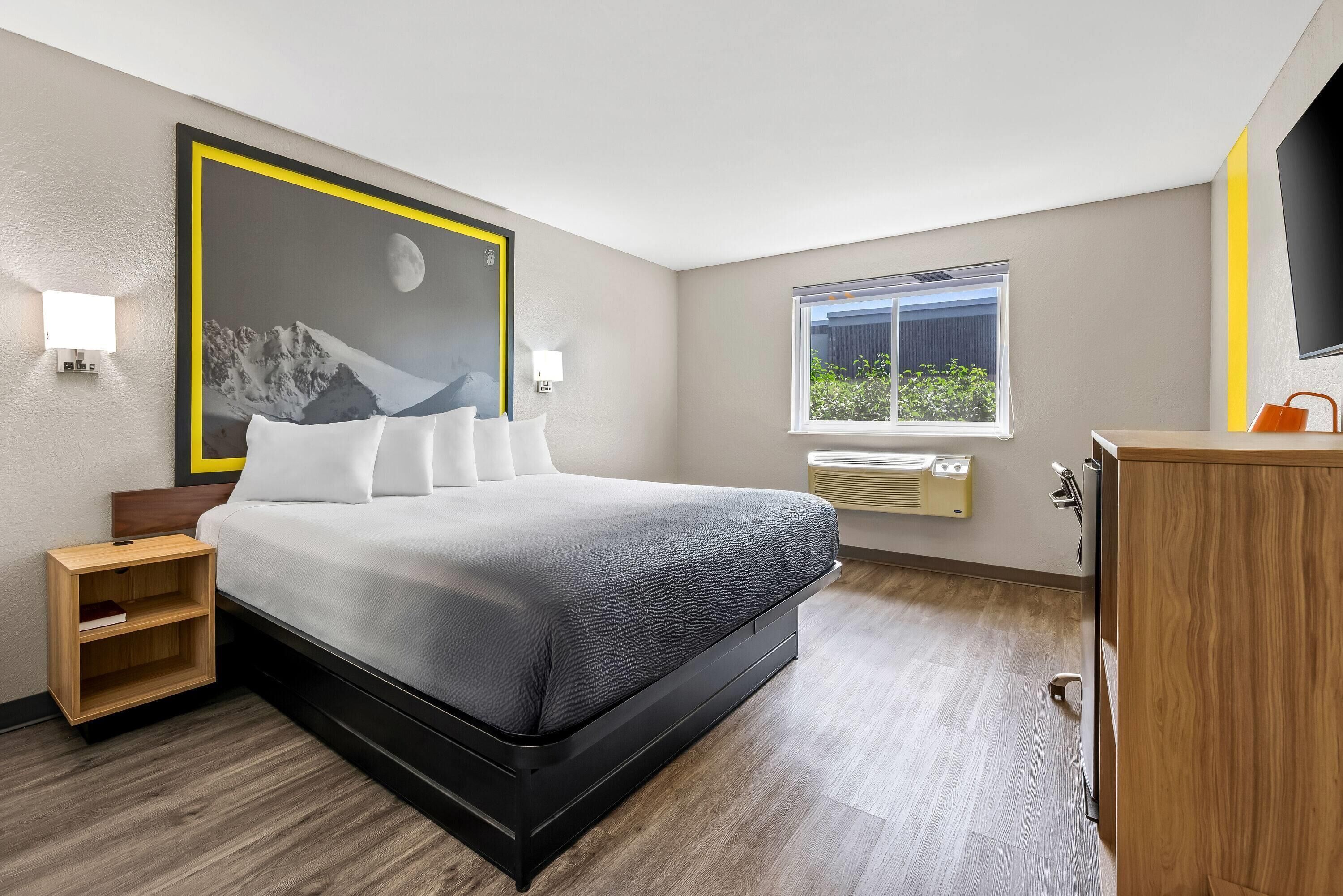 A modern hotel room with a large bed, bedside tables, a window with a view, and a wall-mounted TV.