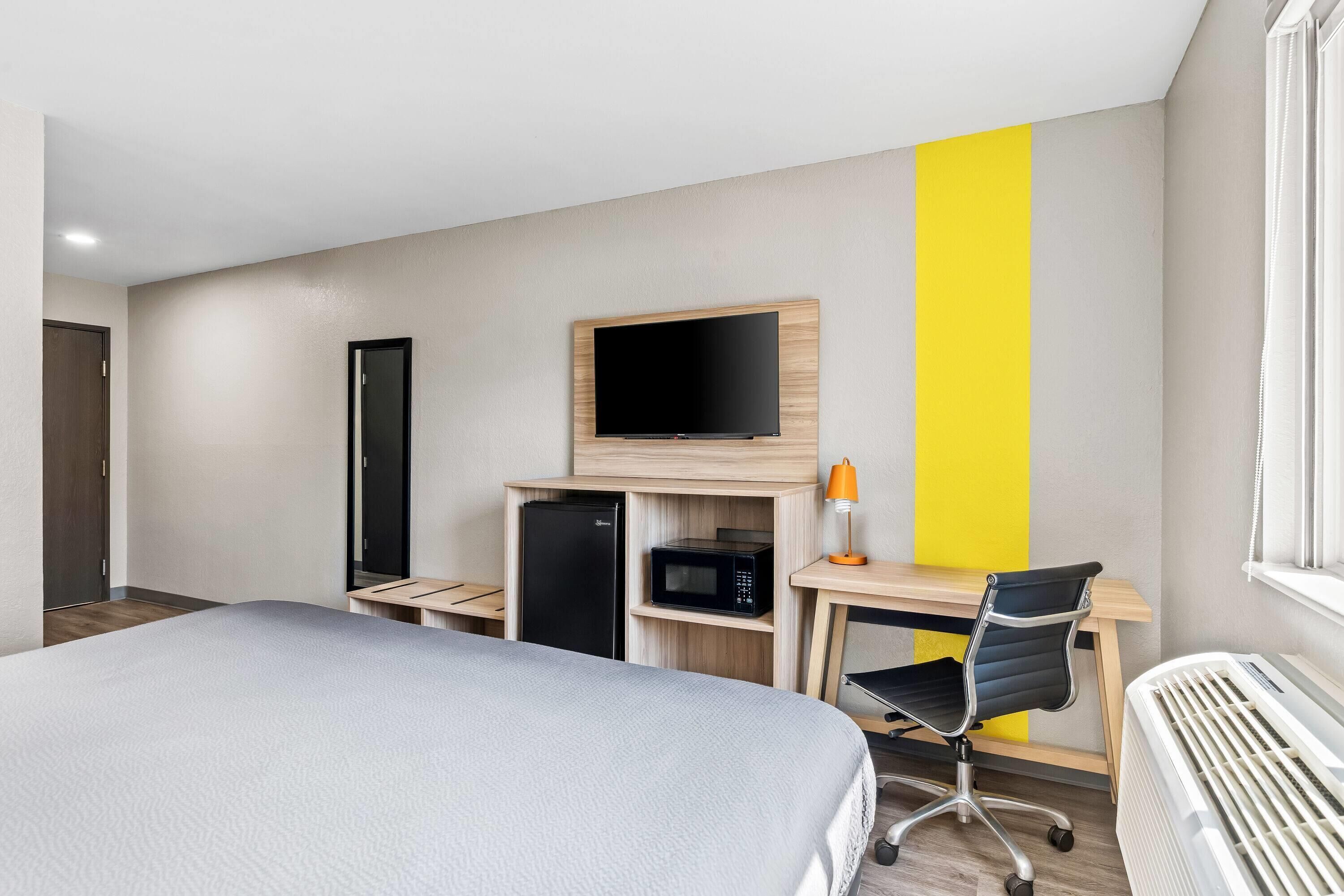 A hotel room with a bed, a desk with a computer, a TV, a microwave, and a heater.