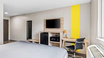 A hotel room with a bed, a desk with a computer, a TV, a microwave, and a heater.