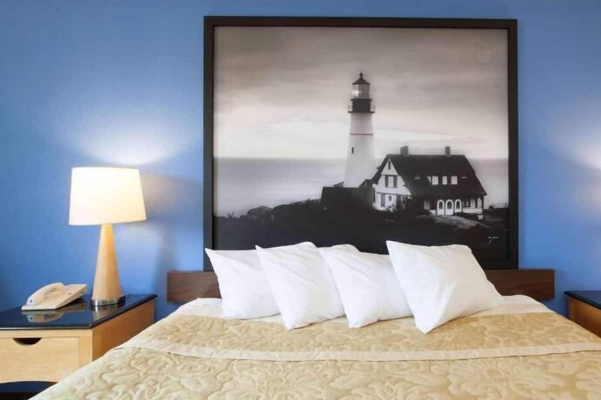 Ein Hotelzimmer mit einem Bett, zwei Nachttischen, zwei Lampen und einem Bilderrahmen mit einem Leuchtturm.
