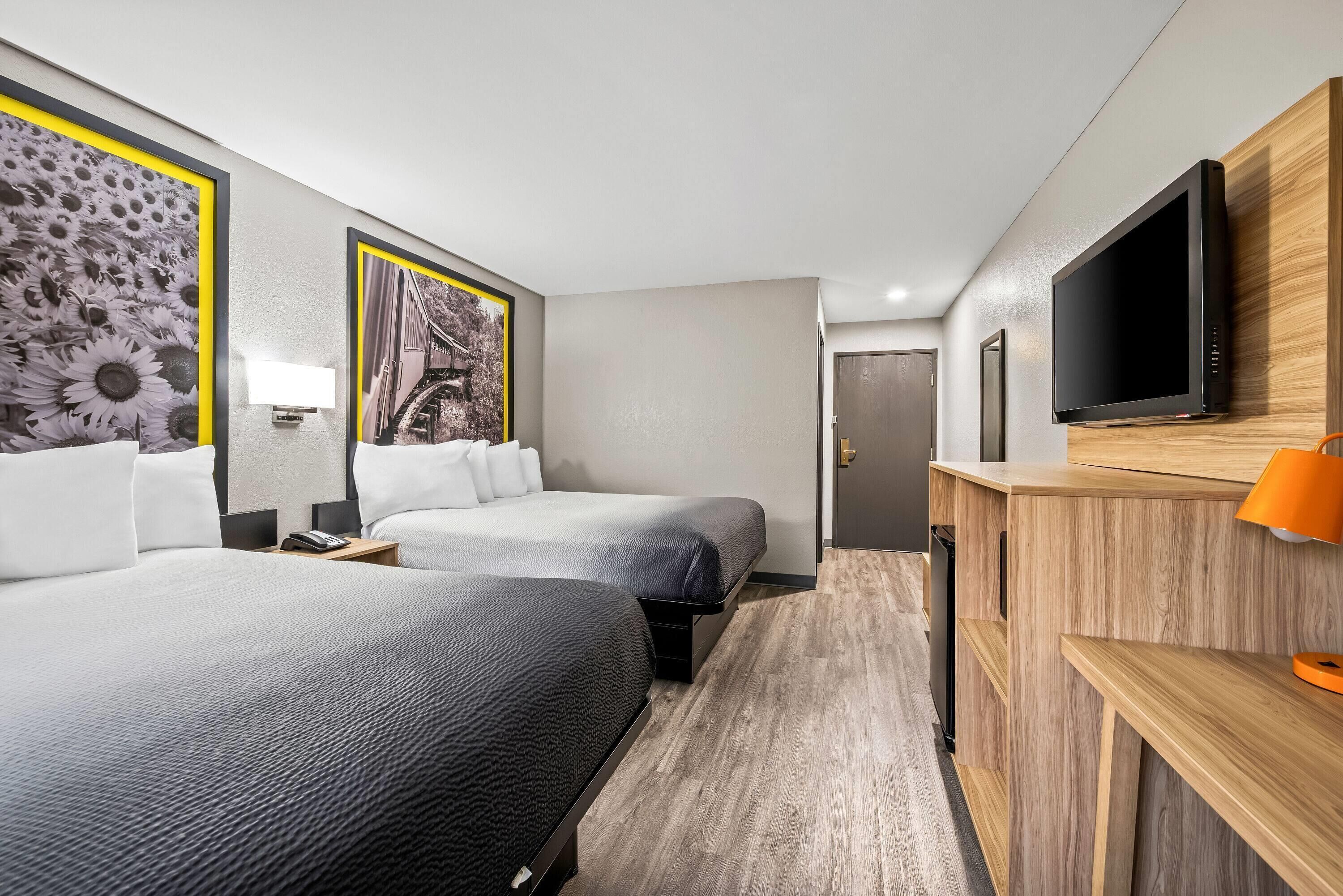 A hotel room with two beds, a TV, a wooden desk, and artwork on the walls.