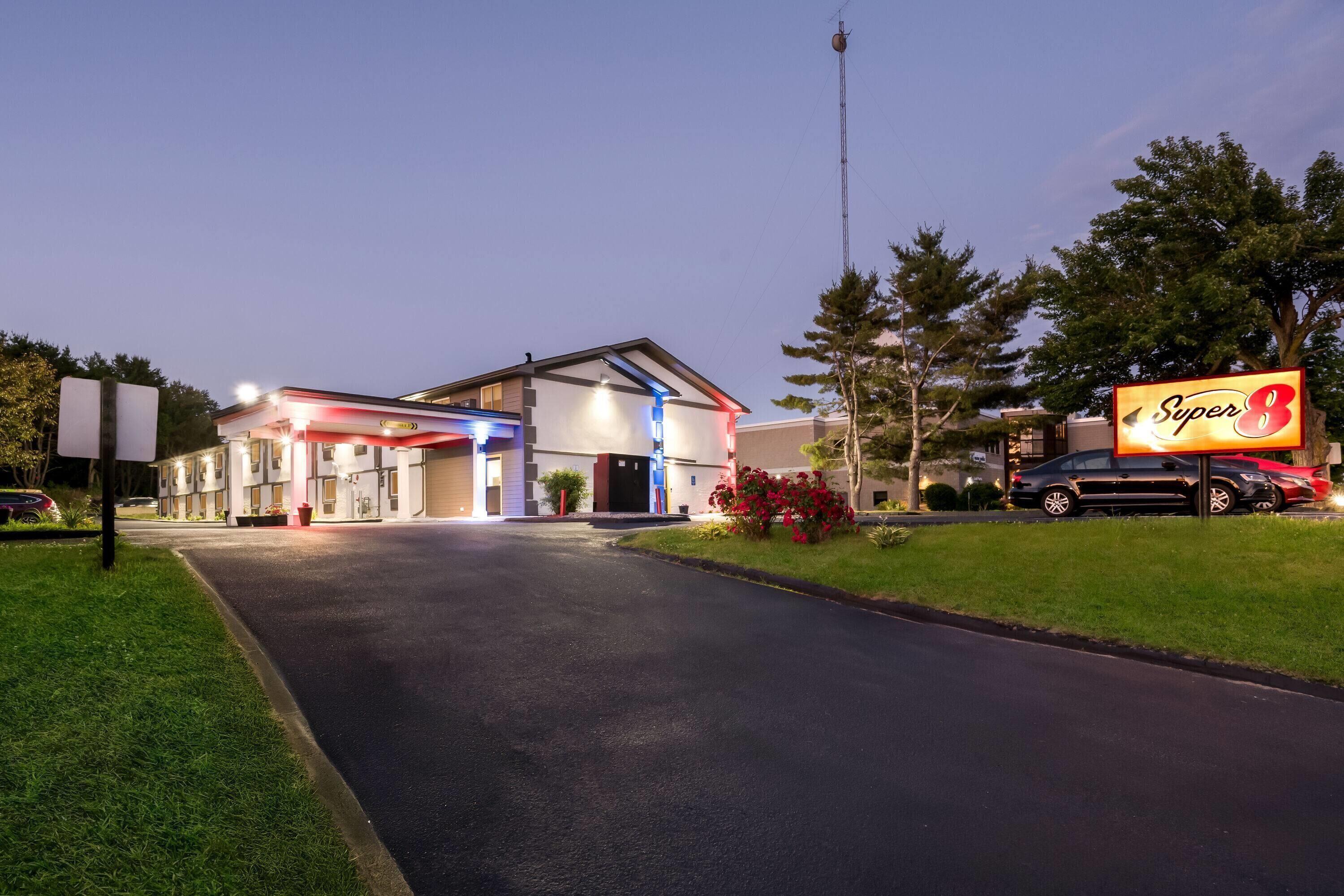 Een hotel met een goed verlichte ingang, een groot bord en een parkeerplaats met auto's.
