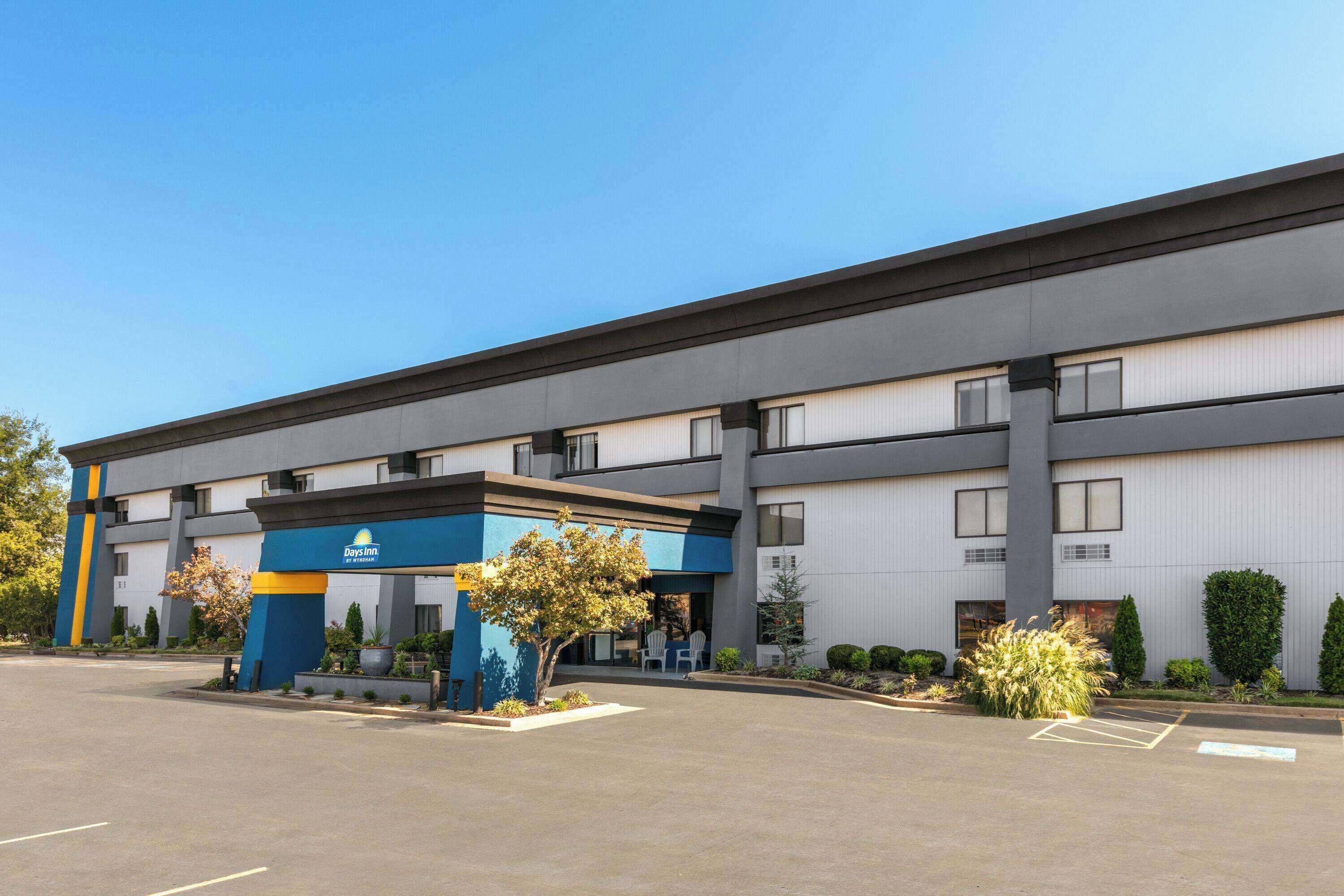 A Days Inn hotel with a modern exterior, a parking lot, and a small landscaped area with a tree and shrubs.