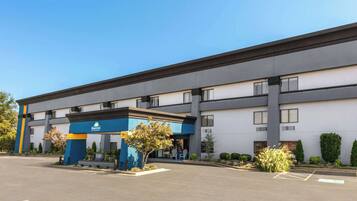 Een Days Inn hotel met een moderne gevel, een parkeerplaats en een klein aangelegd gebied met een boom en struiken.