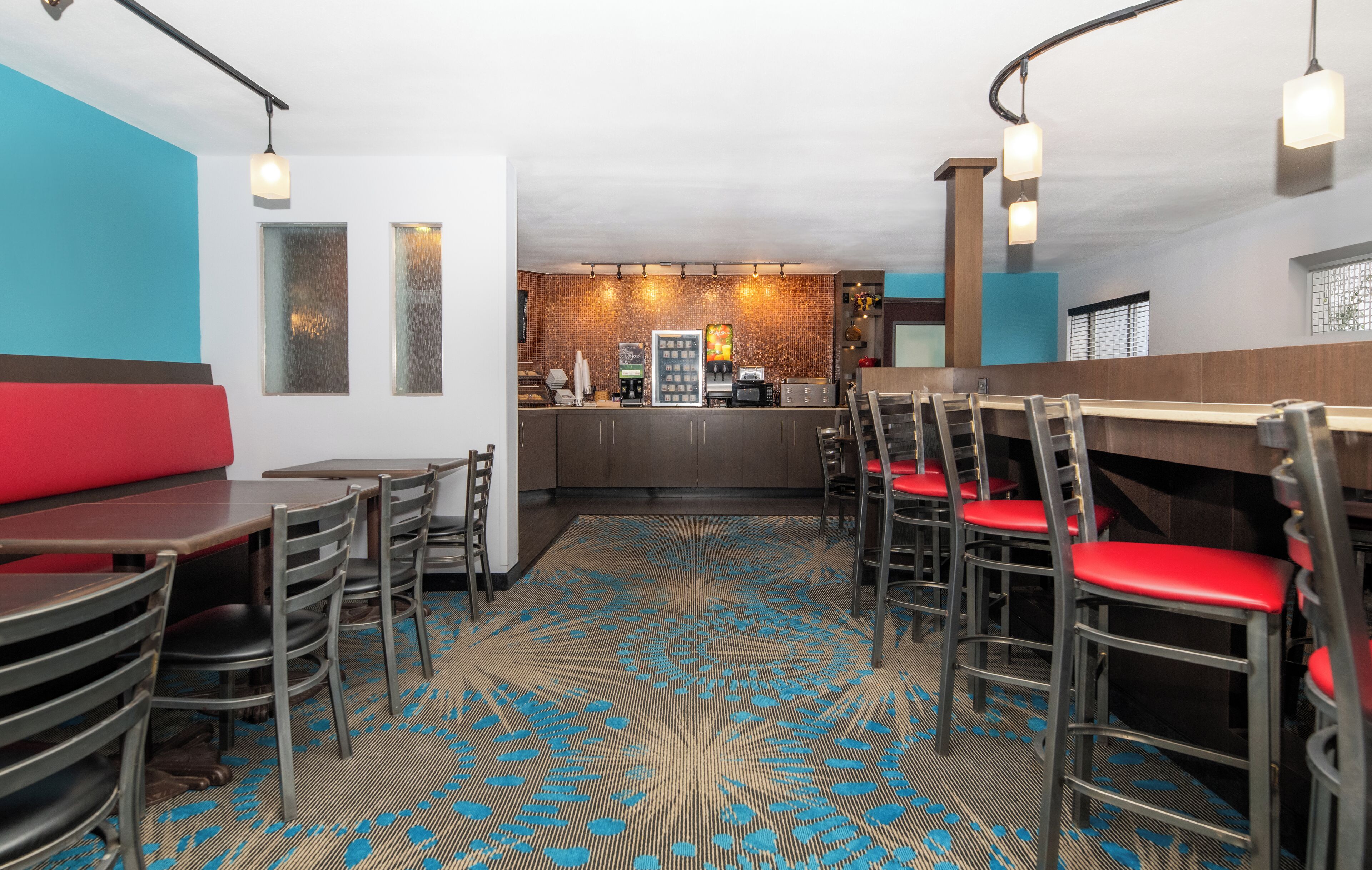 Un restaurante con mostrador, asientos acolchados rojos y alfombra estampada.