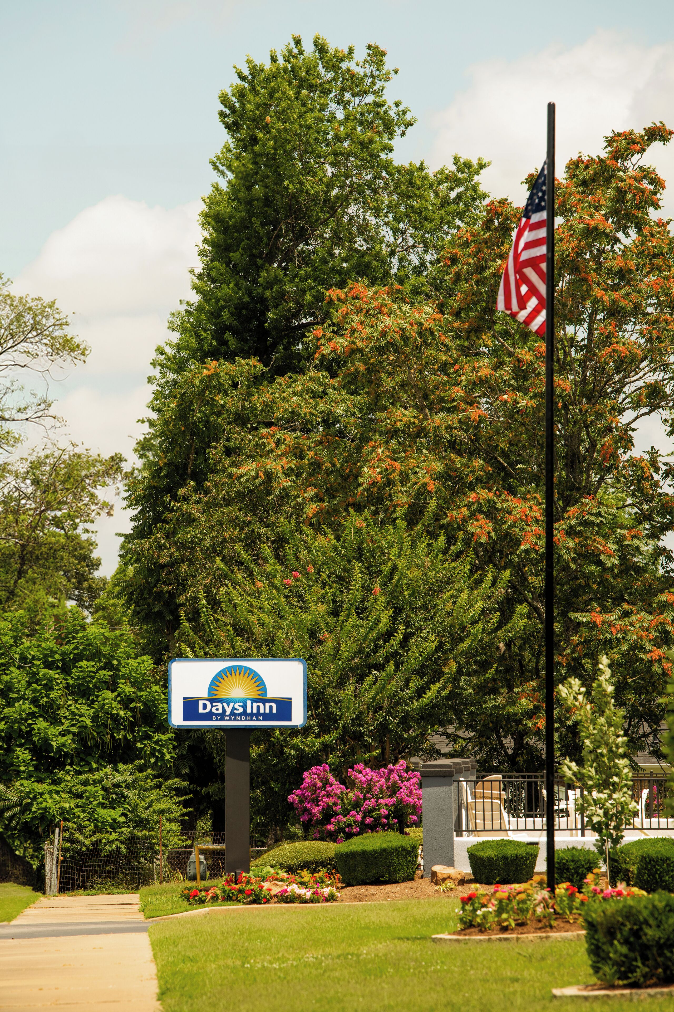 A Days Inn sign with a flagpole and American flag, surrounded by lush greenery and flowering plants.