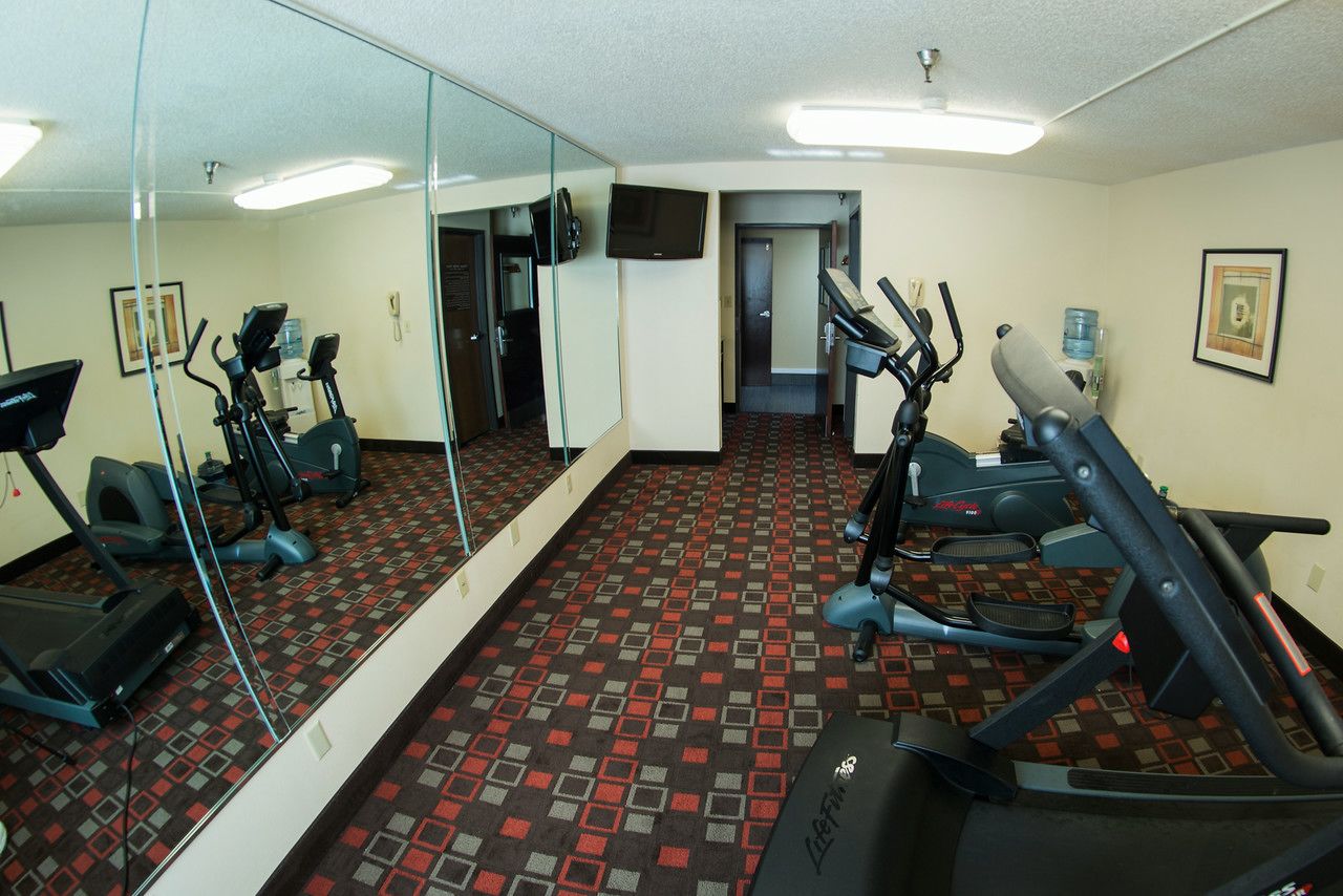 A gym with exercise equipment, a large mirror, and a patterned carpet.
