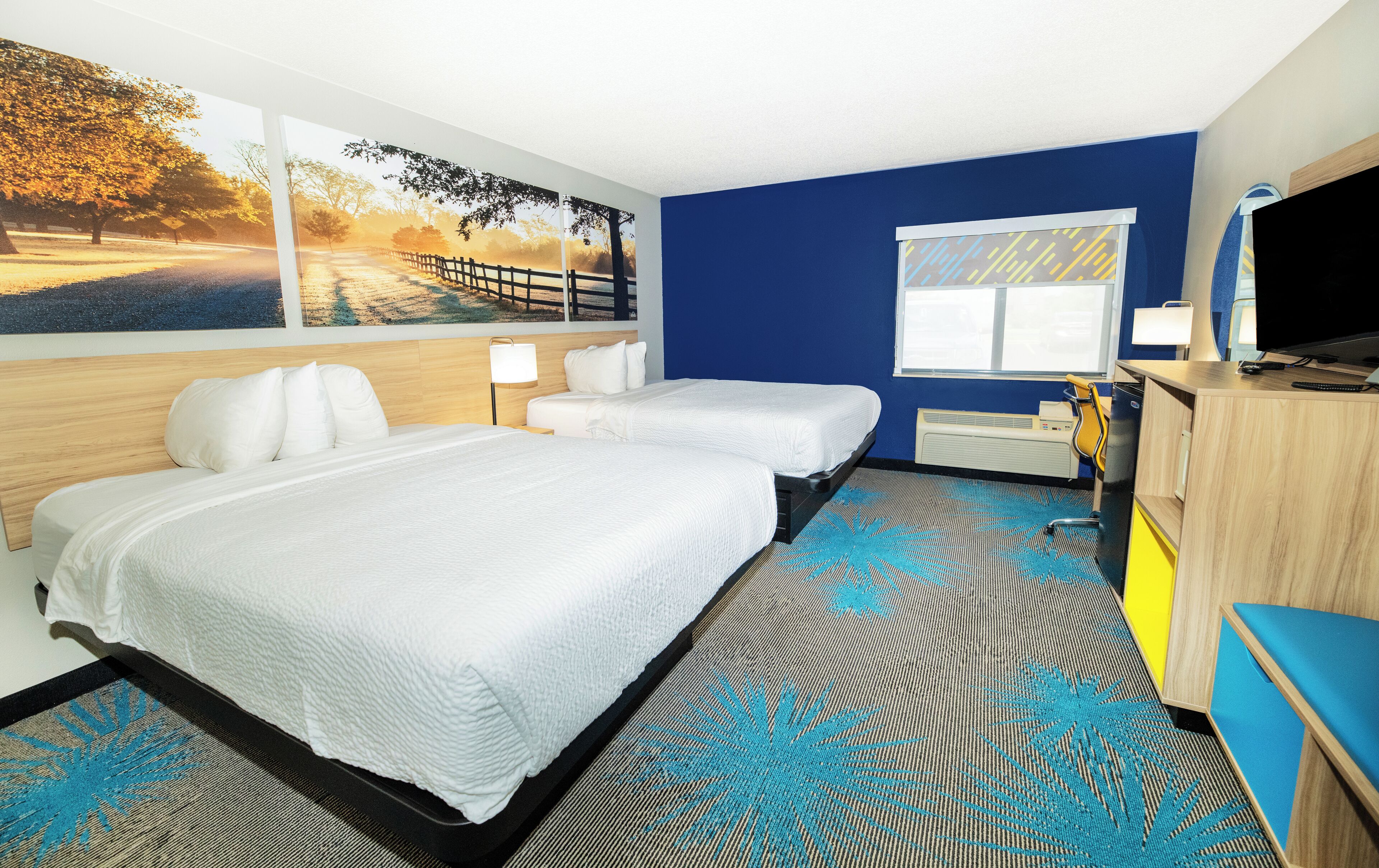Habitación de hotel con dos camas, un escritorio, un televisor y una ventana.