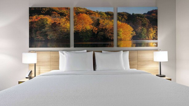 A hotel room with a large bed, two bedside lamps, and a wall-mounted painting of autumn foliage. - Days Inn by Wyndham Fort Smith (Fort Smith)