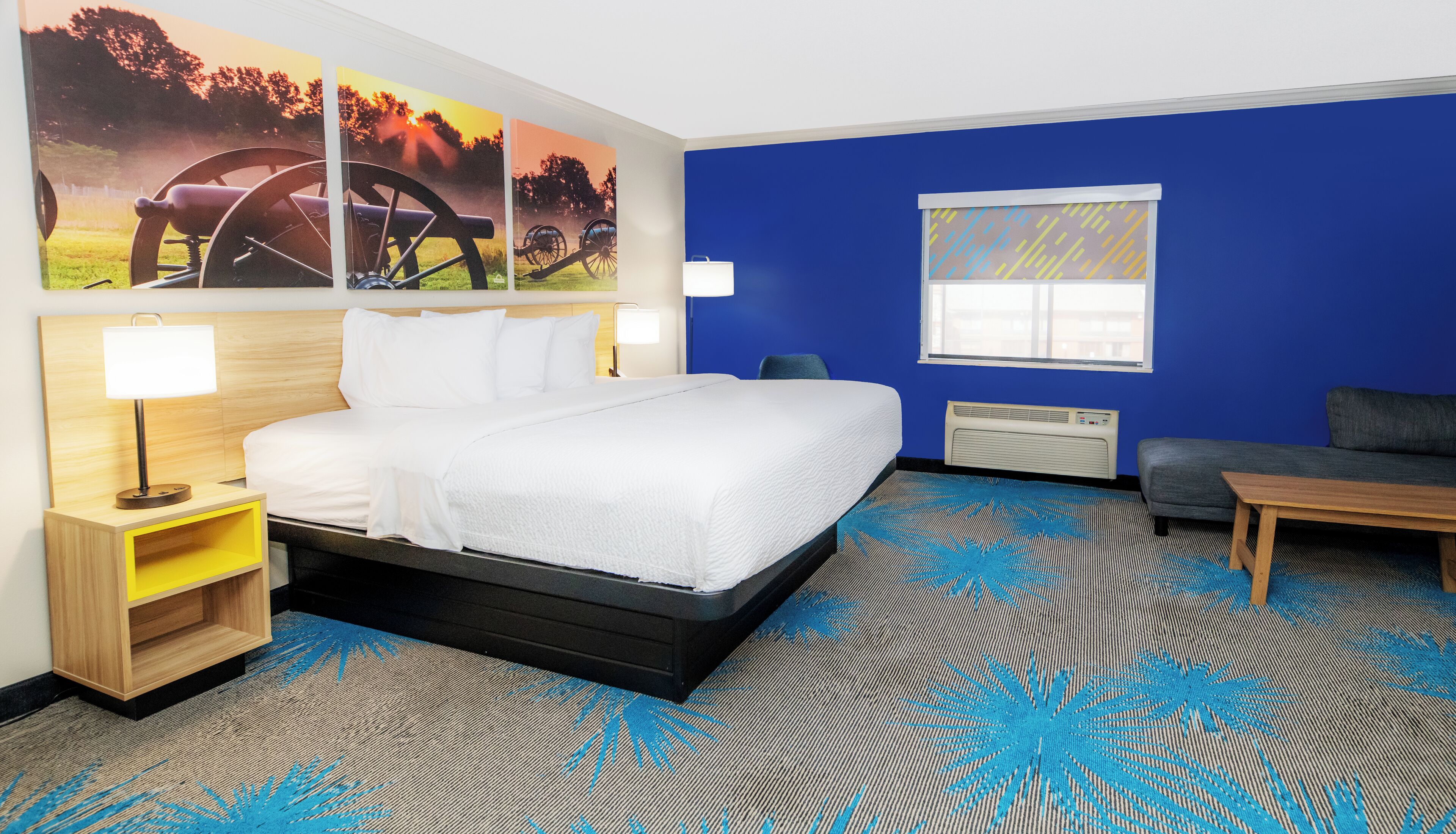 A hotel room with a bed, bedside table, lamp, and a large window.