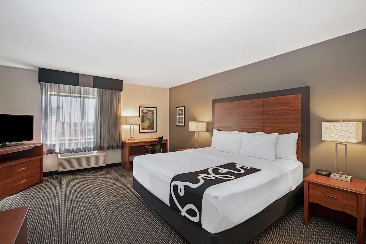 A hotel room with a large bed, a desk, a chair, a TV, and a window with curtains.
