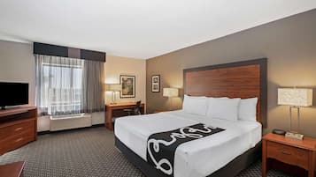 A hotel room with a large bed, a desk, a chair, a TV, and a window with curtains.