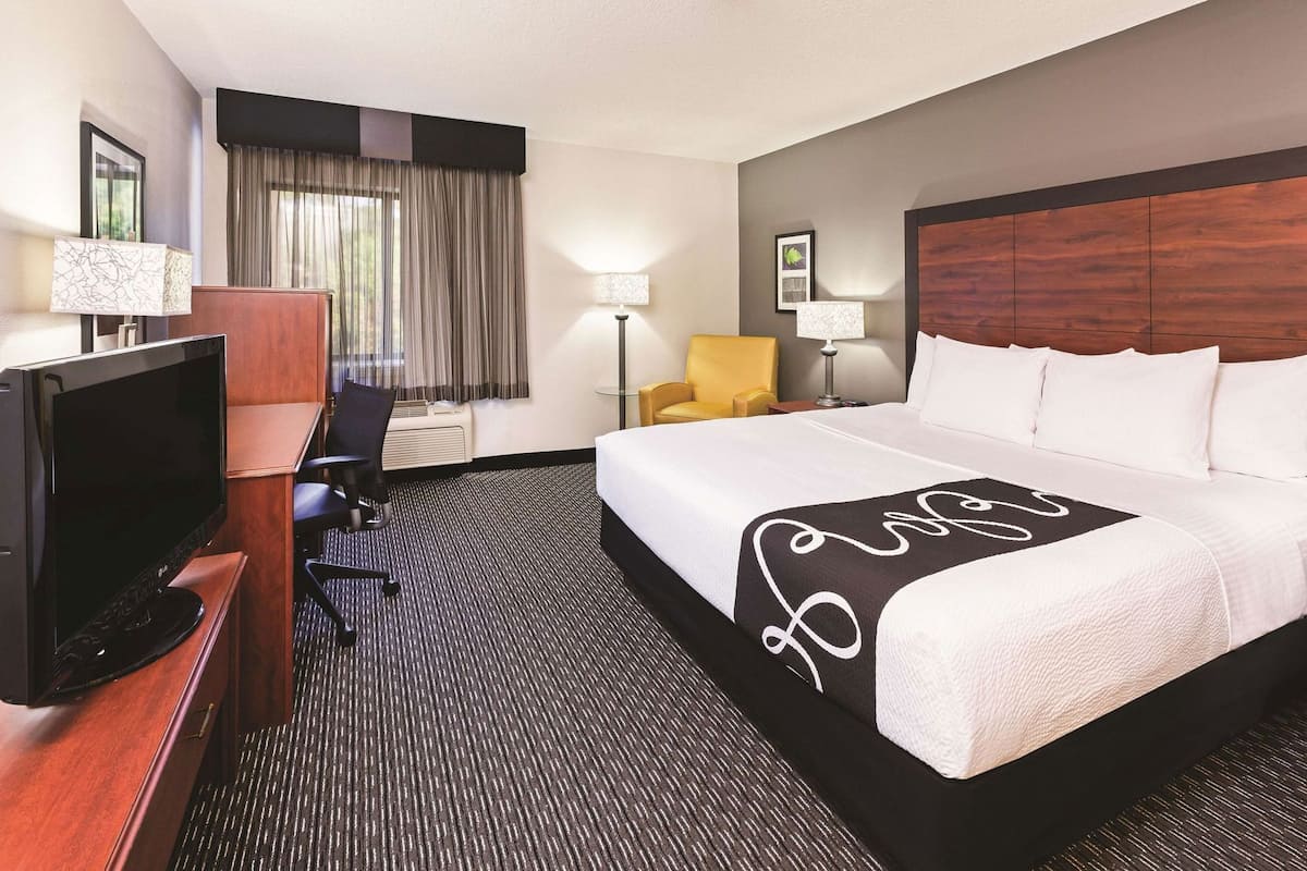 A hotel room with a bed, a desk with a TV, a chair, and a lamp.