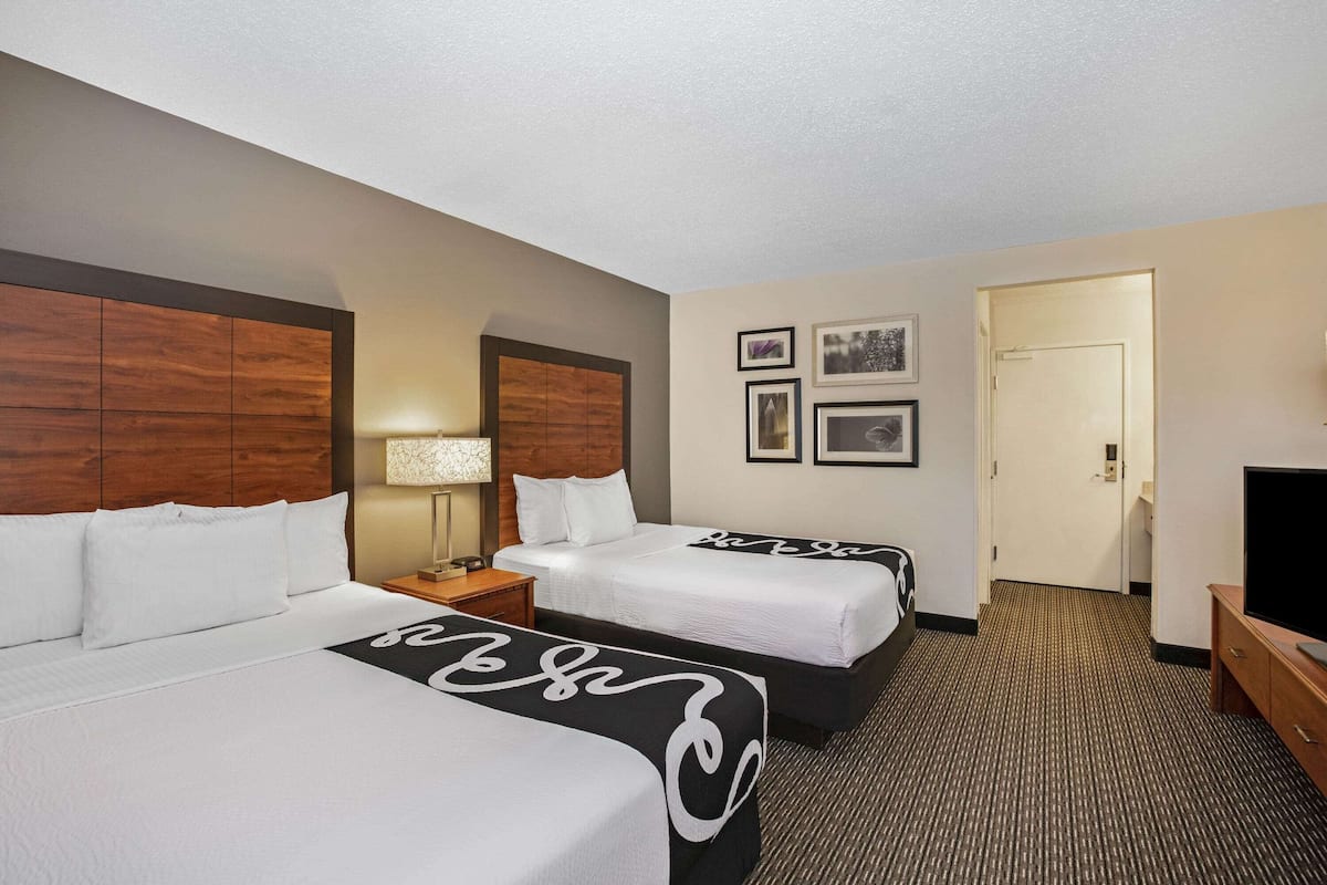 A hotel room with two beds, a TV, a lamp, and framed pictures on the wall.