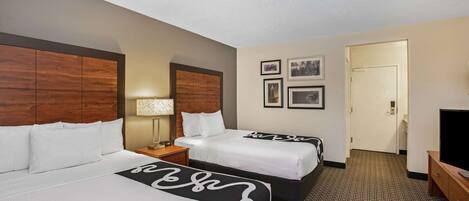 A hotel room with two beds, a TV, a lamp, and framed pictures on the wall.