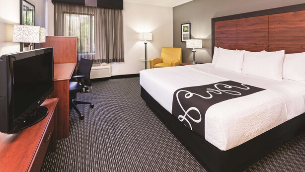 A hotel room with a large bed, a desk with a TV, a chair, and a lamp. - La Quinta Inn & Suites by Wyndham N Little Rock-McCain Mall (North Little Rock)