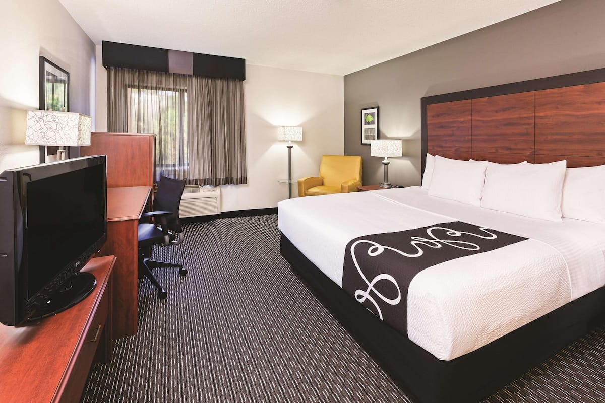 A hotel room with a large bed, a desk with a TV, a chair, and a lamp.