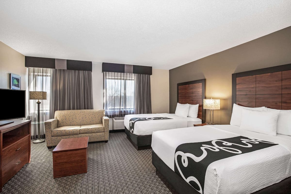 A hotel room with two beds, a sofa, a TV, a lamp, and a desk.