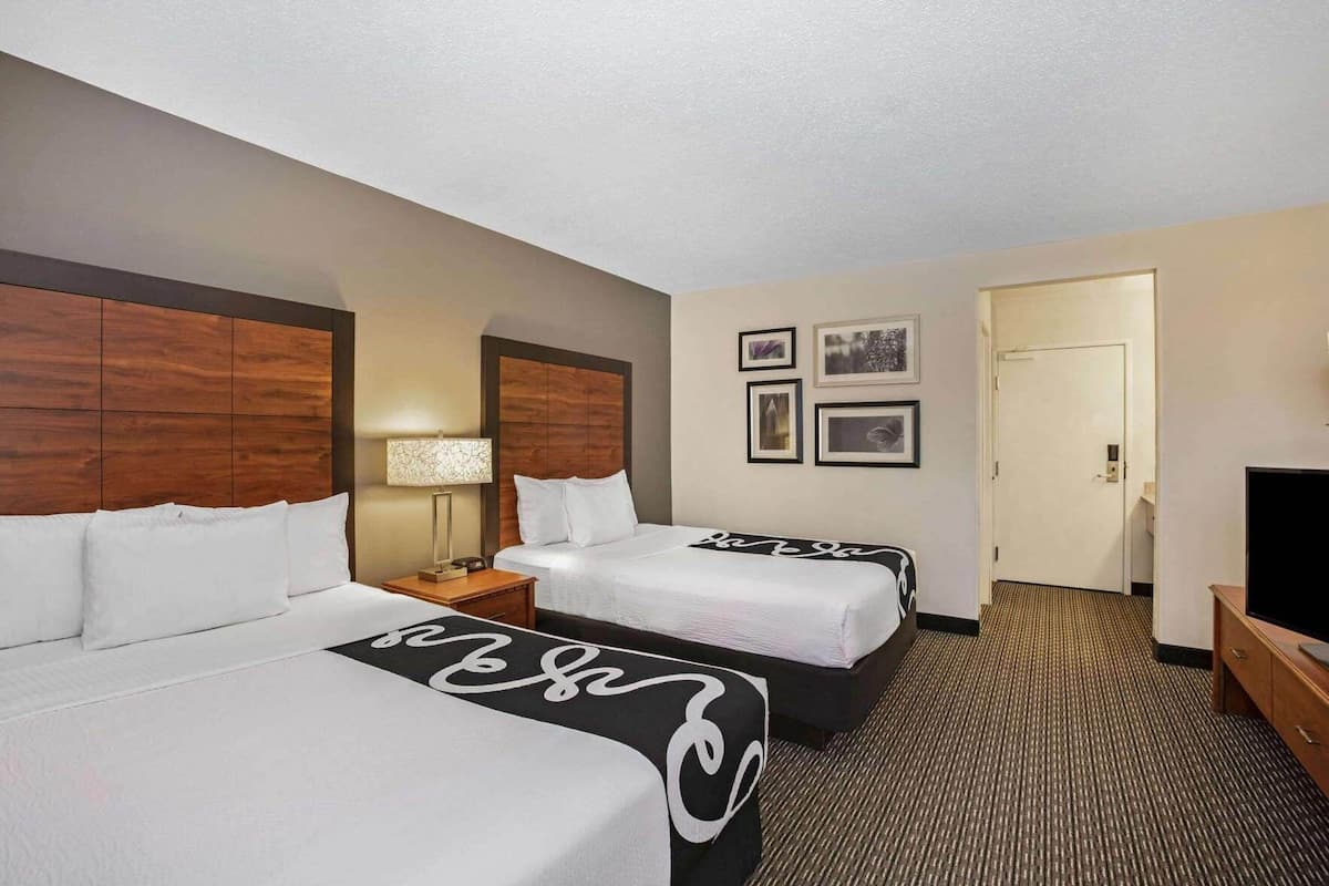 A hotel room with two beds, a TV, a desk, and a door.